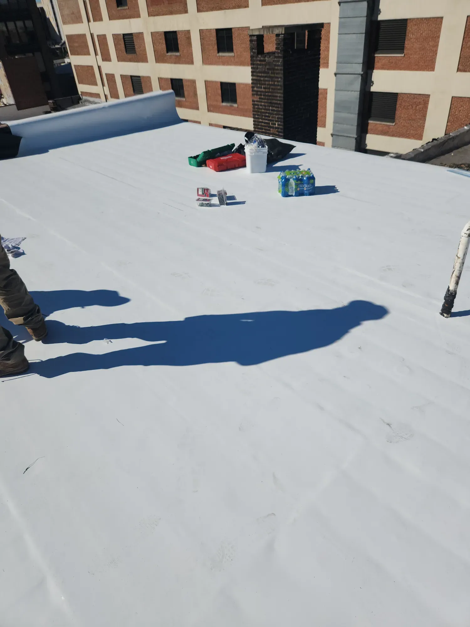 White single-ply membrane on a flat roof, with a roll of membrane and tools